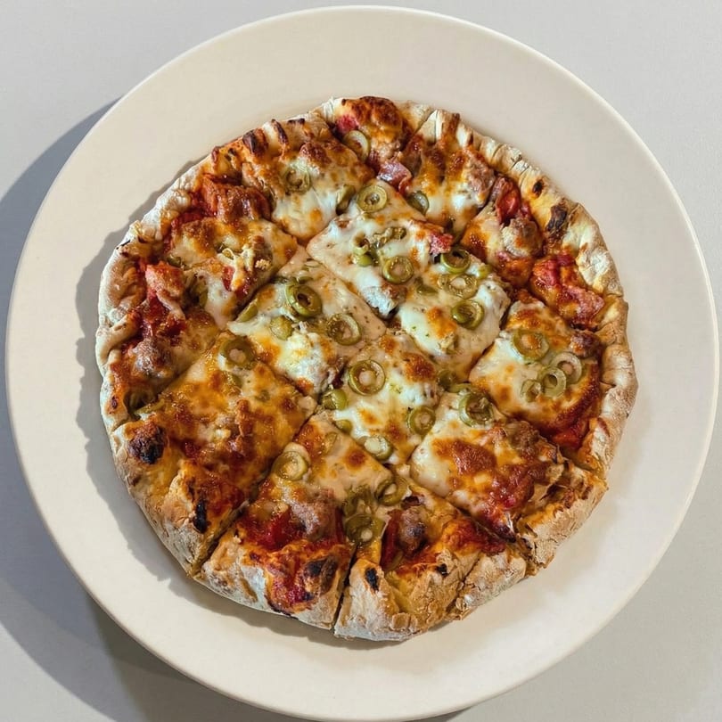 A whole, sliced pizza with melted cheese, tomato sauce, and green olives on a white plate.